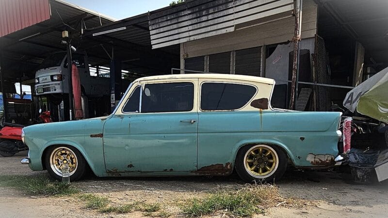 Ford Anglia 105E in blue and cream color, rust covered panels and gold aftermarket wheels.